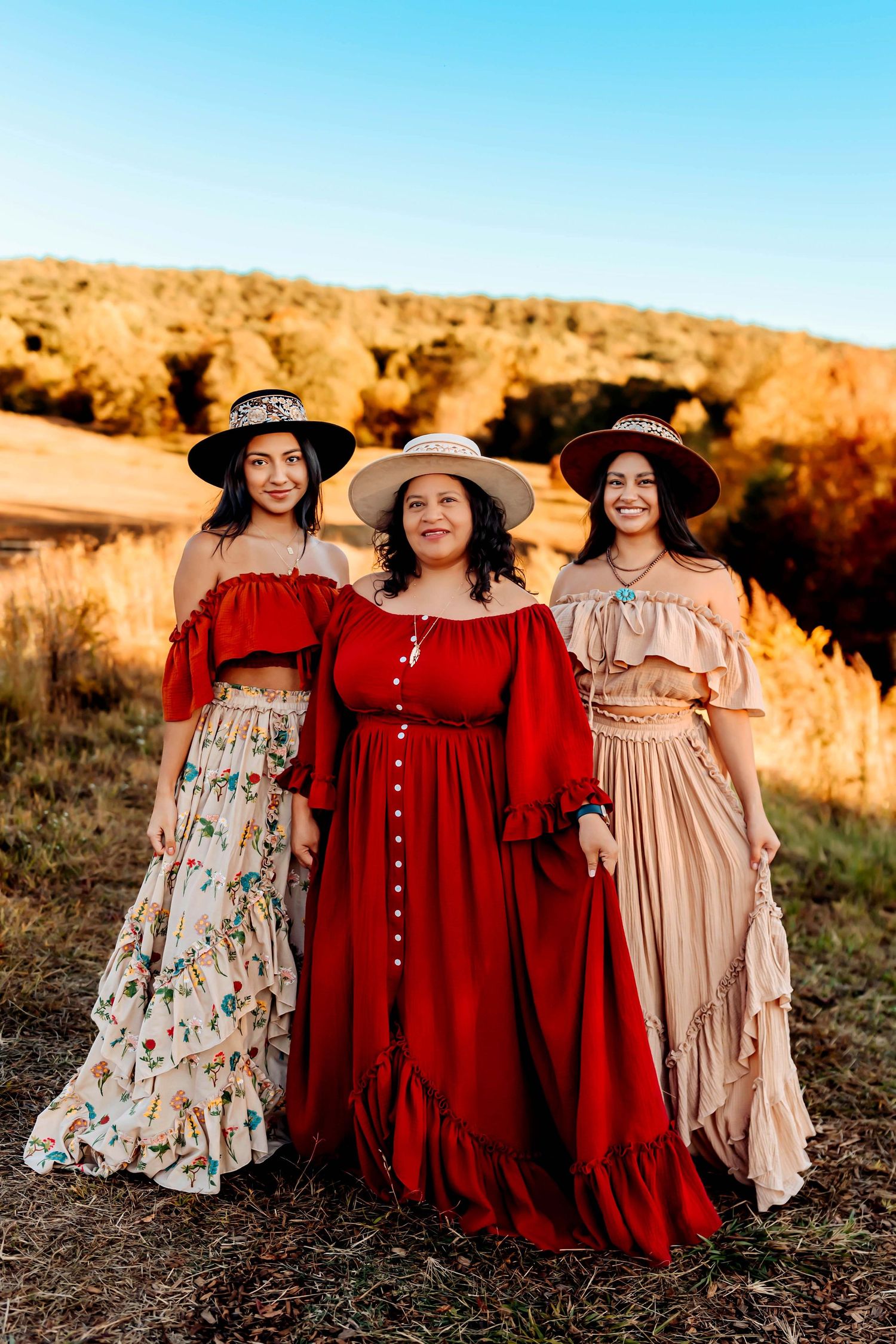 Three women in vintage-style prairie dresses and wide brim hats posing against desert landscape.