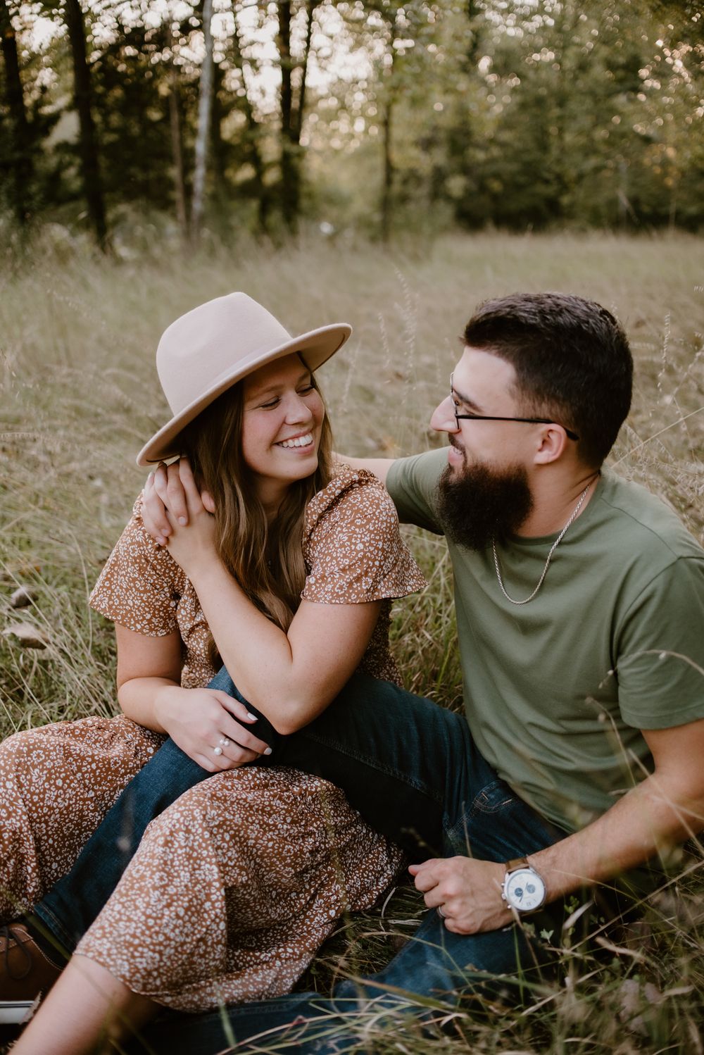 A couple lounges together on grass sharing intimate moments during an outdoor photoshoot.