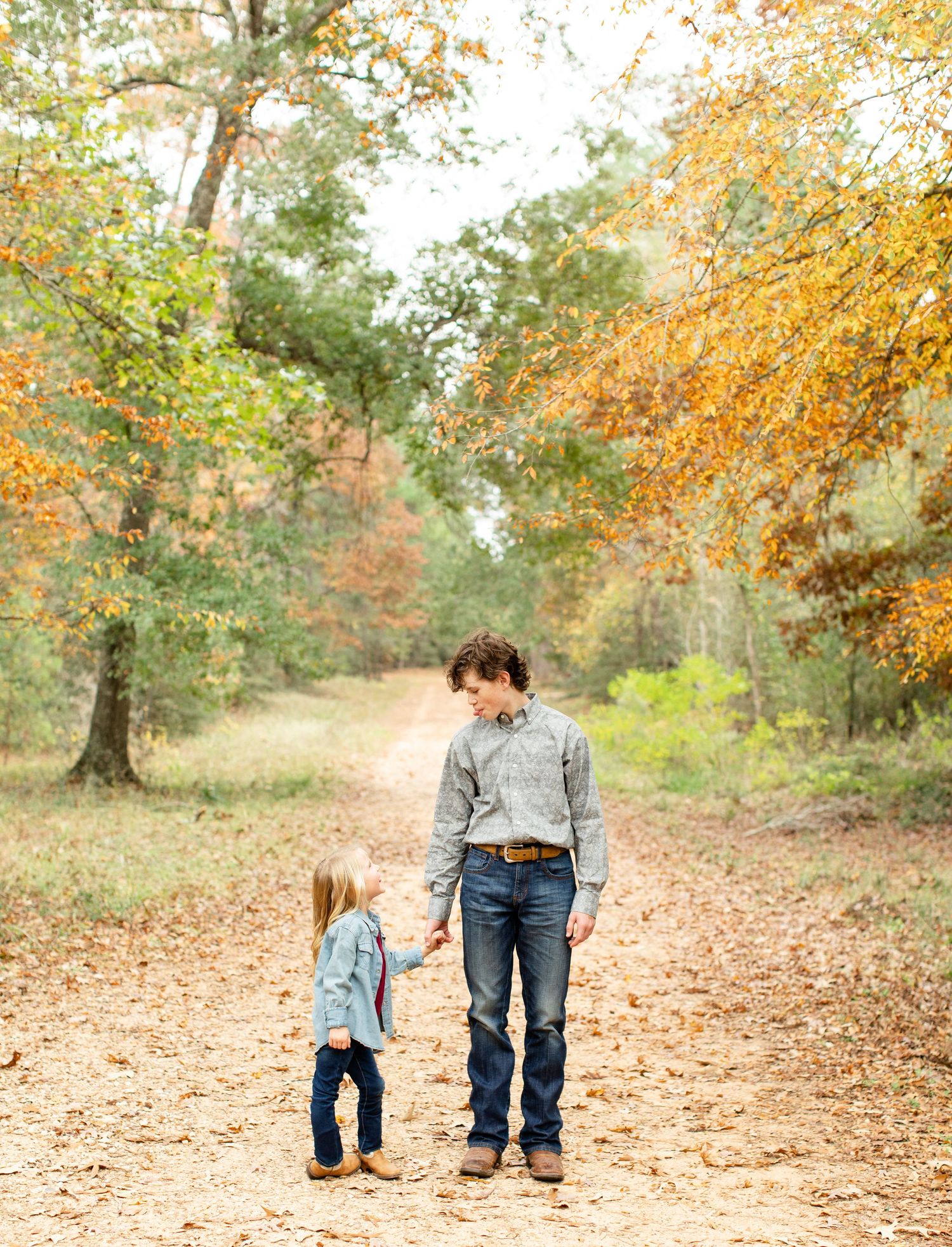 Two people walking hand in hand down a wooded trail covered in autumn leaves.