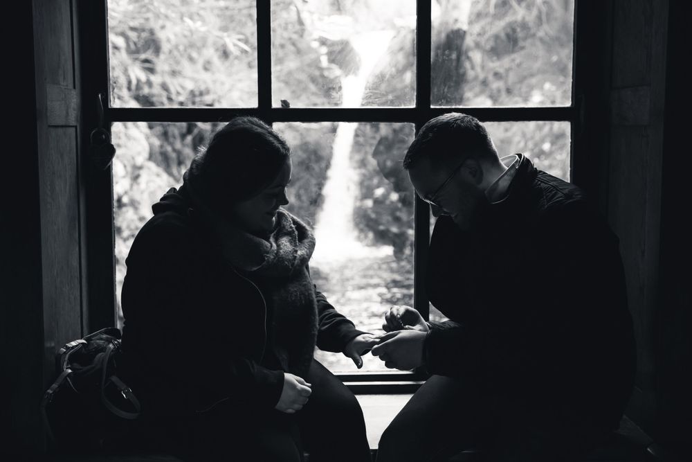 Silhouetted figures sitting by a window with waterfall backdrop in black and white.