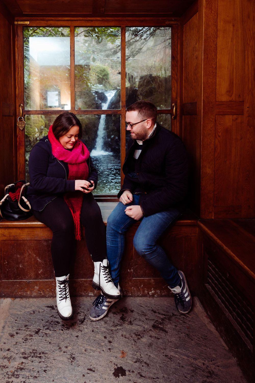 Couple sitting in a wooden window seat with a waterfall view behind them.