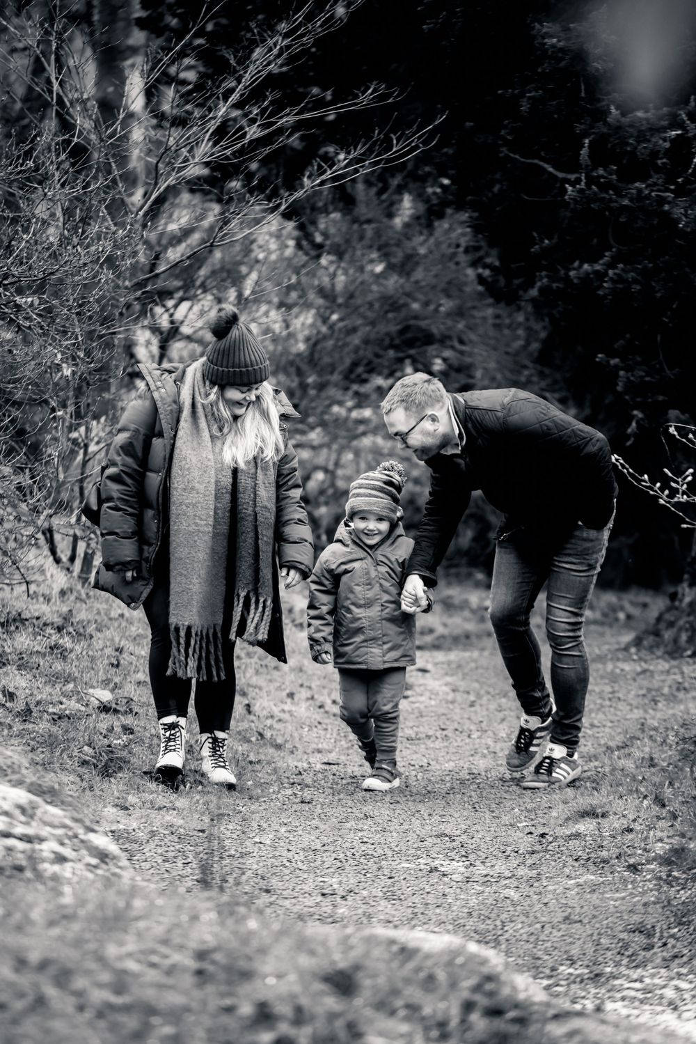 Family walking together on a woodland path in black and white.