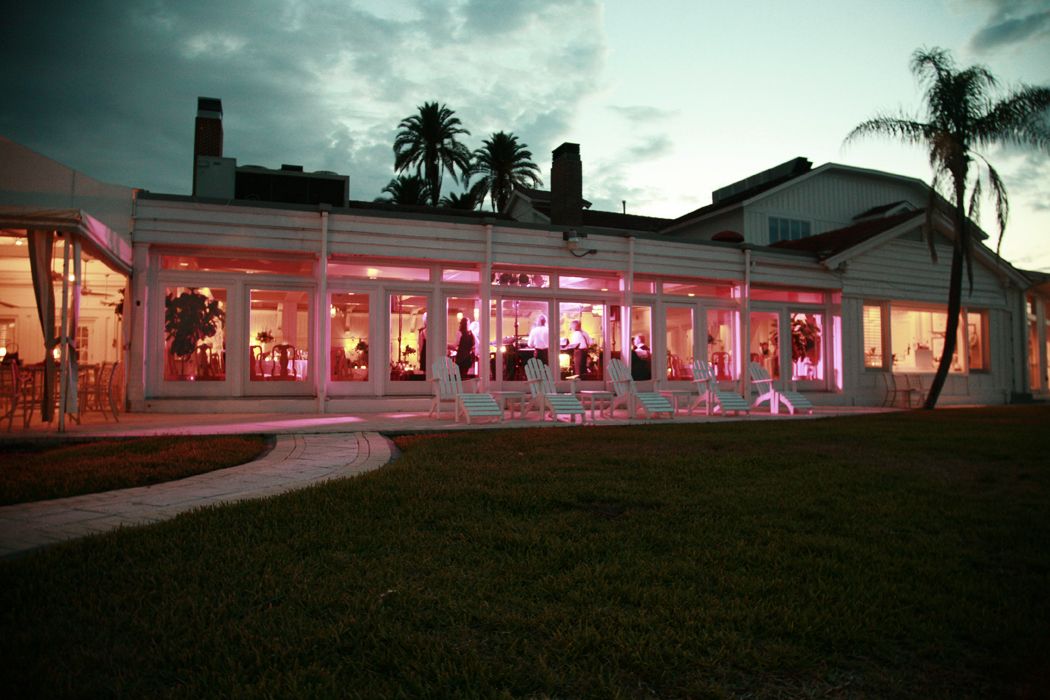 Pink-lit storefront at dusk with palm trees and neon signs glowing against dark sky.