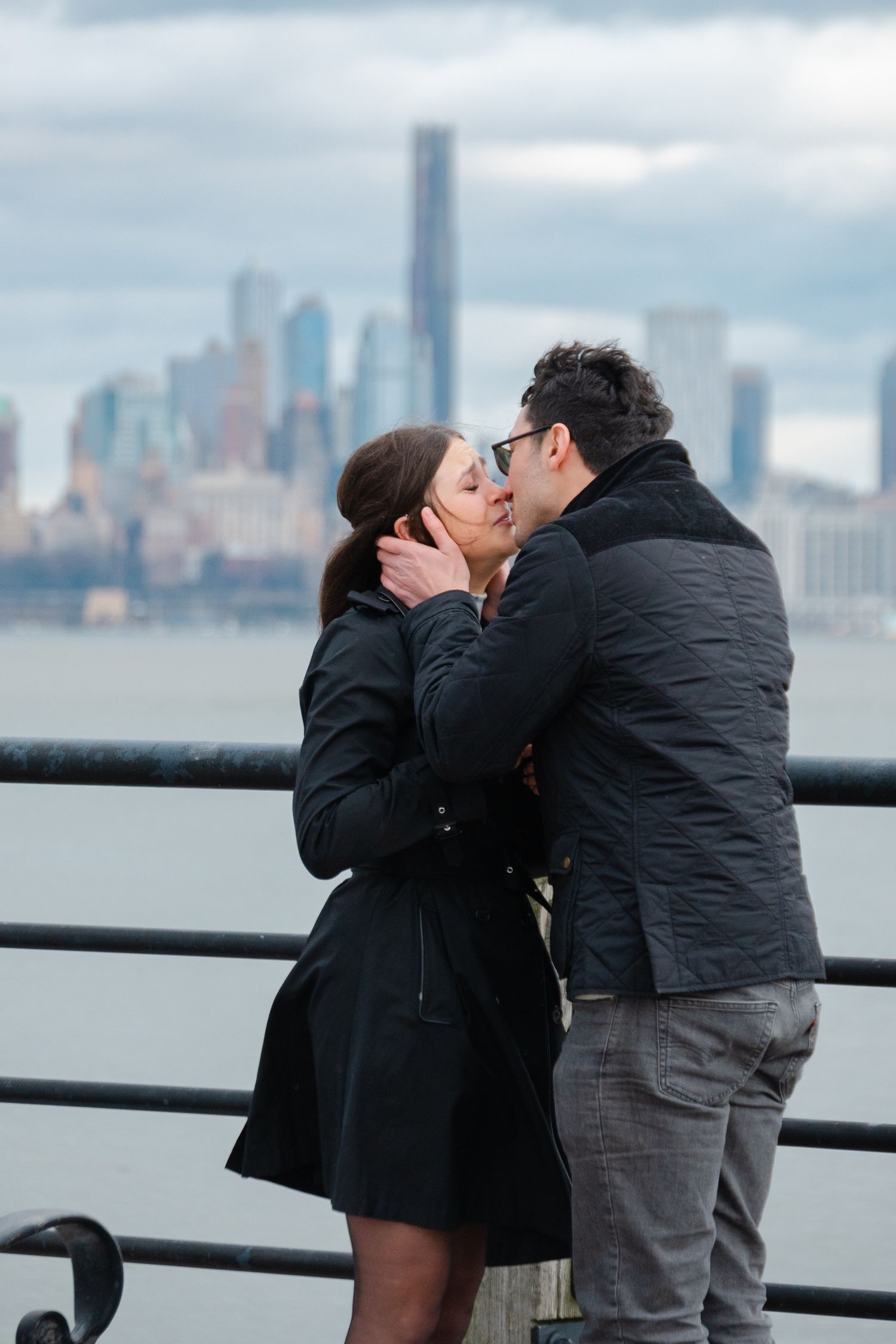 Couple emotionally kissing with NYC skyline and Hudson River in Liberty State Park engagement photos