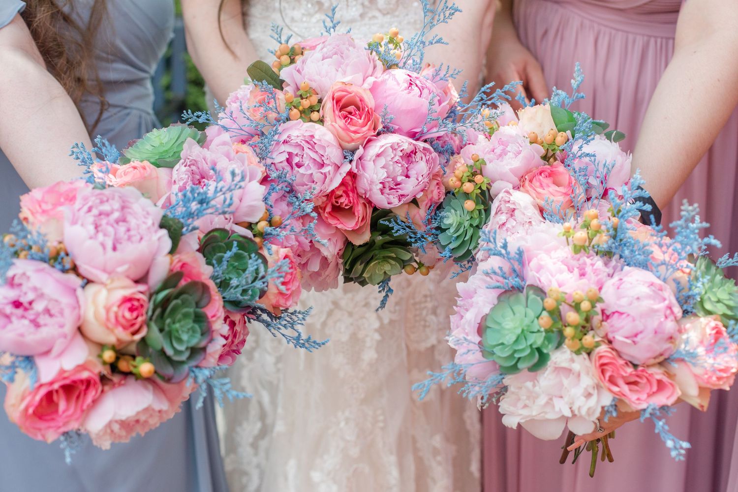 Pink and coral wedding bouquets with roses and peonies held against blush bridesmaid dresses.