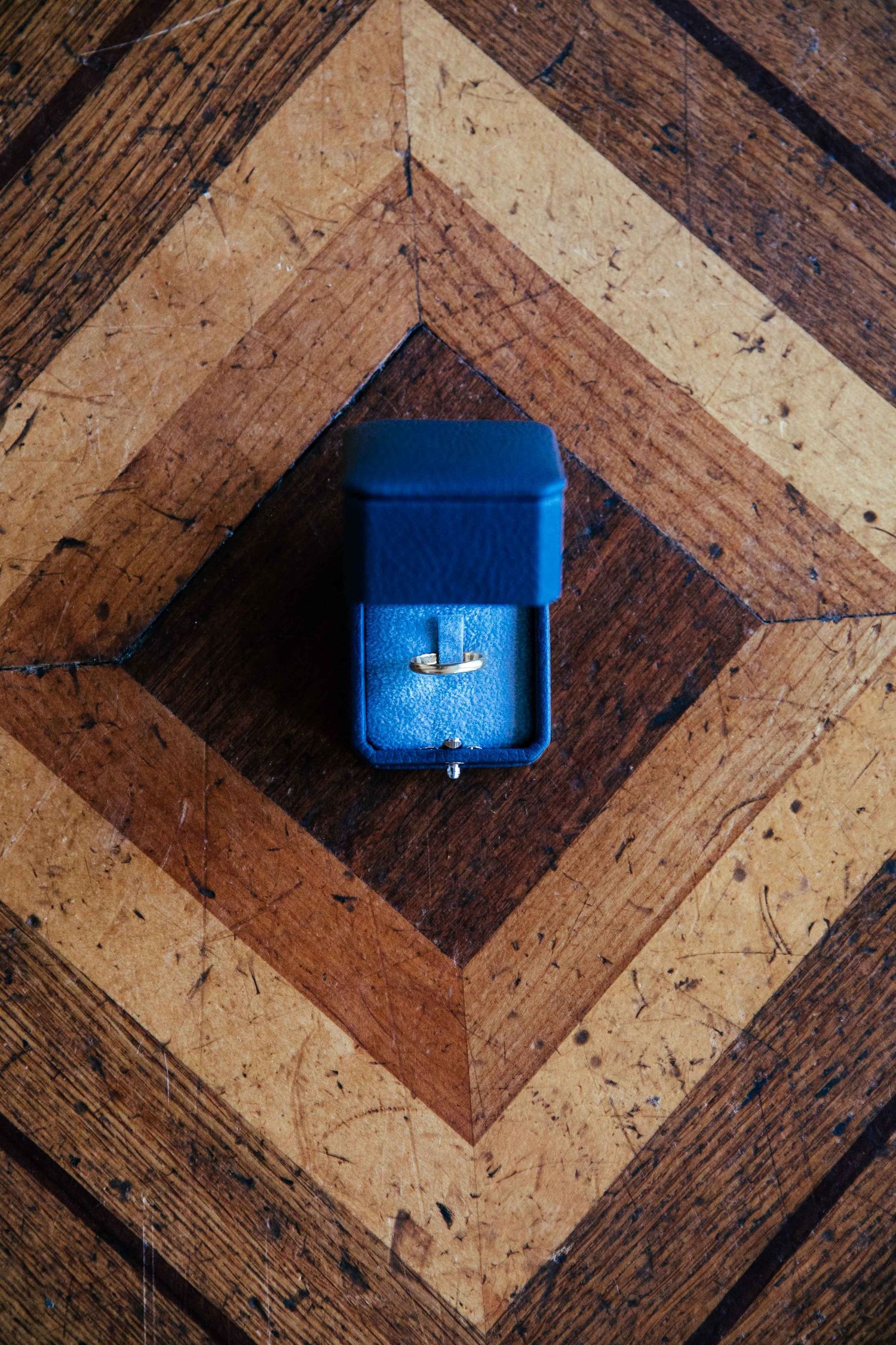 A blue velvet ring box positioned on a geometric wooden parquet floor pattern.