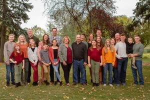 A large group wearing red and neutral colors poses together outdoors during autumn.