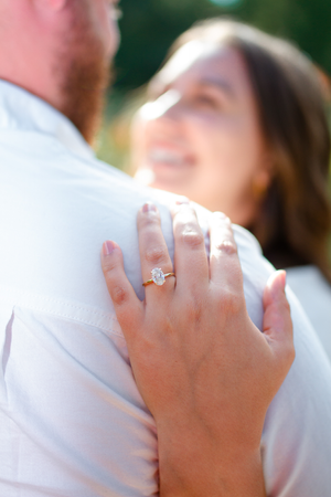 Close-up view of a sparkling engagement ring on a hand pressed against white fabric outdoors.