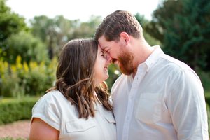 A romantic moment between two people in white clothing outdoors with green foliage in background.