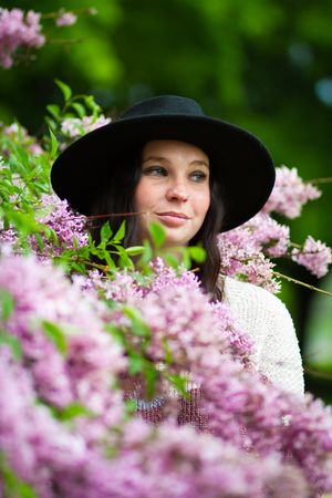 Spring portrait with pink lilac blossoms framing person wearing wide-brimmed black hat.