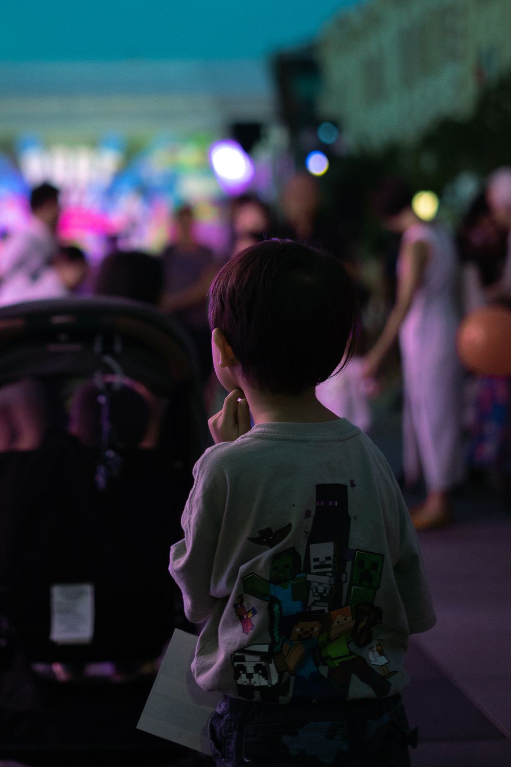 A child watches an evening performance amid a crowd with colorful stage lights in the background.