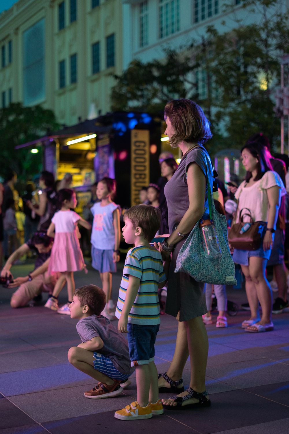 Families gathered at an outdoor evening event with food trucks and city buildings in the background.