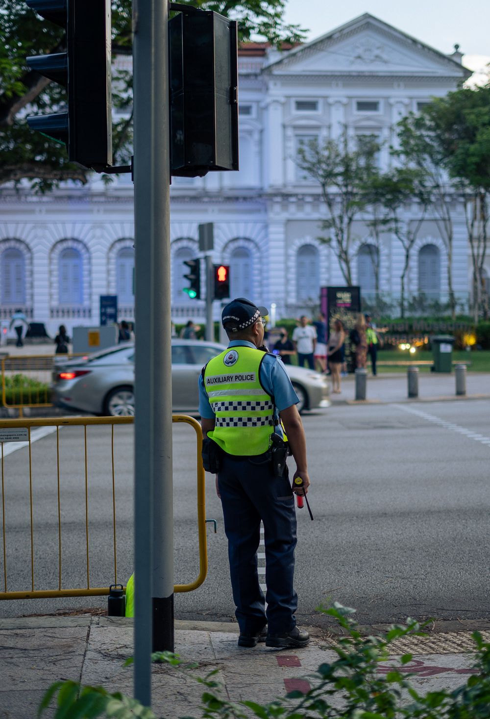 A security officer in reflective vest stands guard near a classic white building.