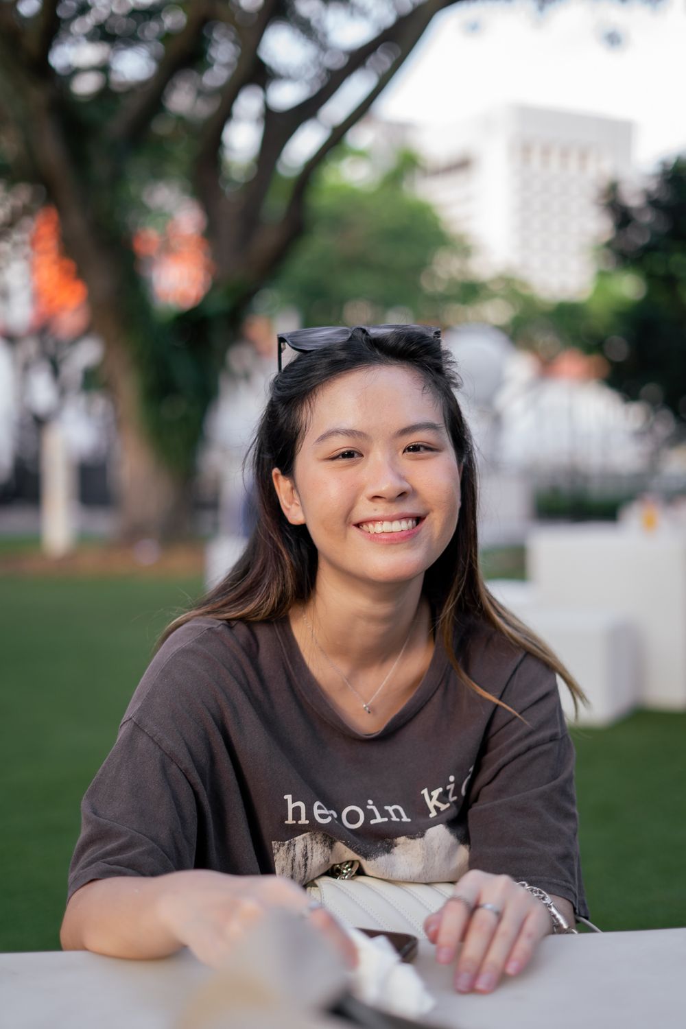 A person sitting outdoors wearing a brown casual t-shirt with sunglasses on head smiles at camera.