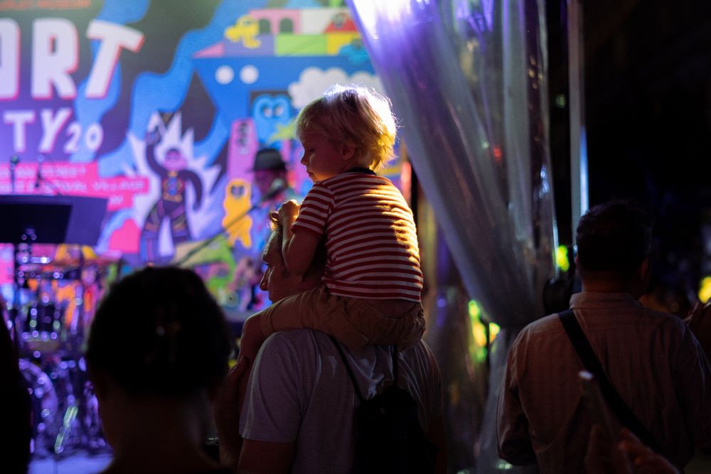 A child sits on shoulders watching an illuminated outdoor display at night.