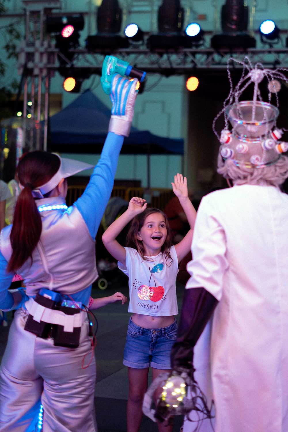 A child dances with performers during an outdoor evening entertainment event with colorful lighting.