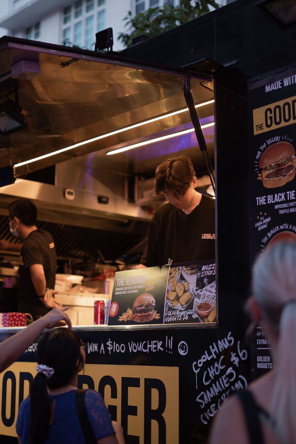 Night view of a burger food truck with menu signs and illuminated service window.