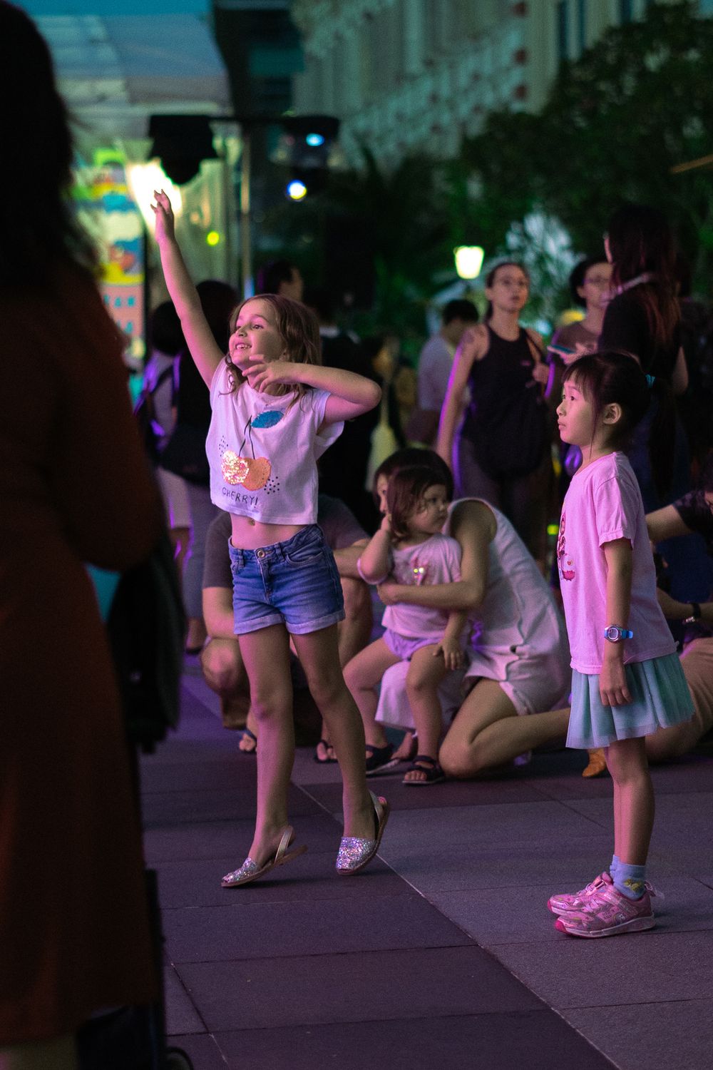 Children dancing and having fun at an outdoor evening event with colorful lighting.