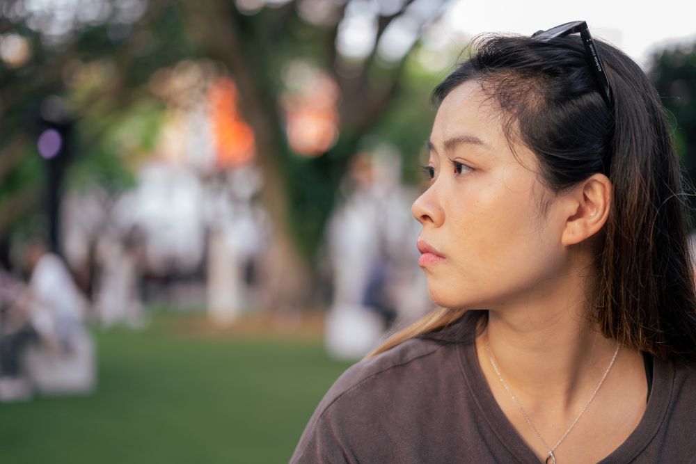 A person in casual attire gazes thoughtfully into the distance in an outdoor park setting.