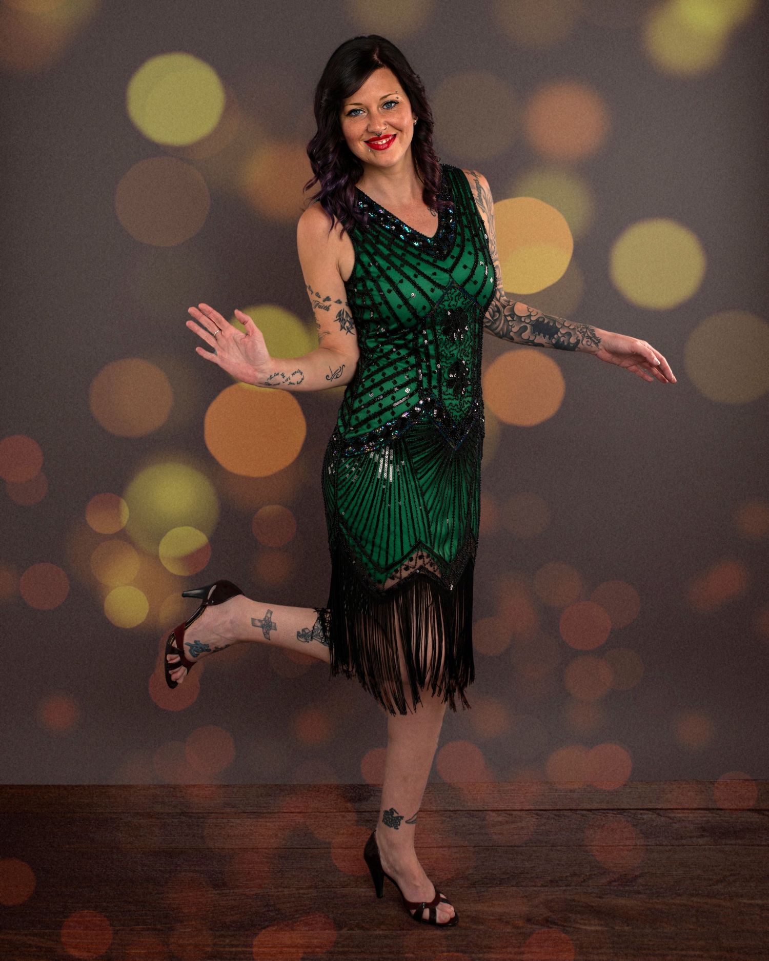 Vintage-style portrait of person in emerald green flapper dress with fringe against bokeh background.