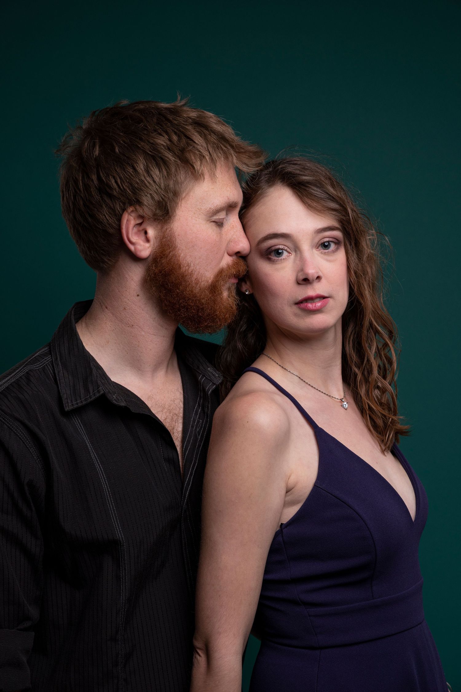 Romantic studio portrait of a couple against a dark green background.