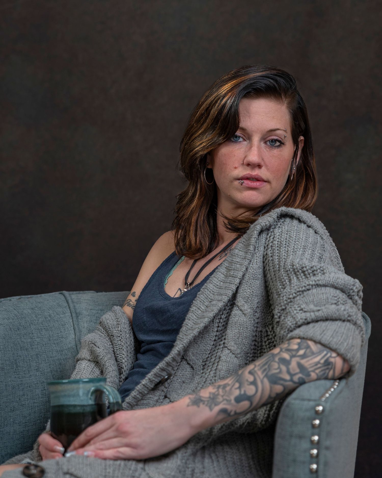 Portrait of person in casual sweater lounging on gray couch with tattoo visible.