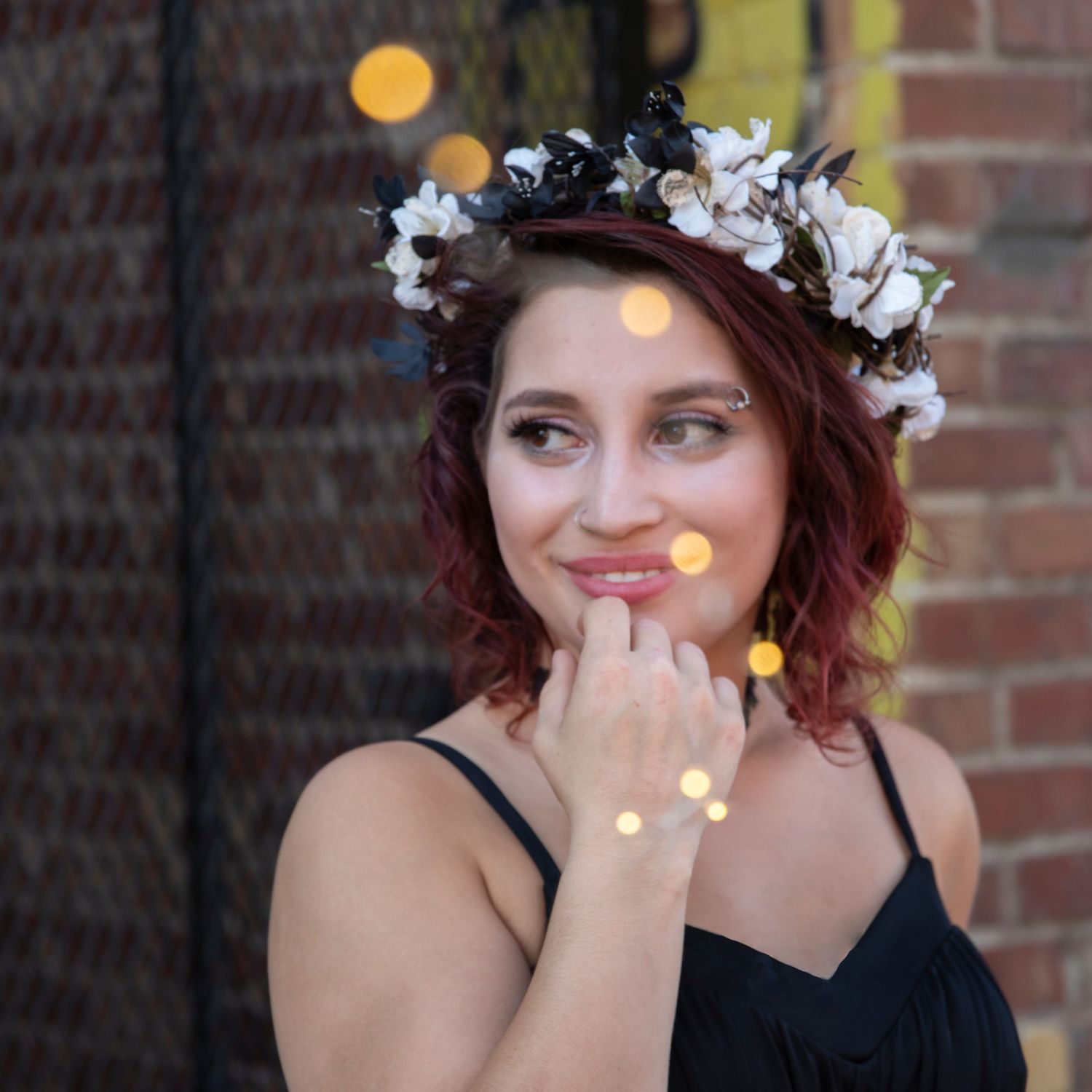 Portrait wearing floral crown with bokeh lights and brick wall background.