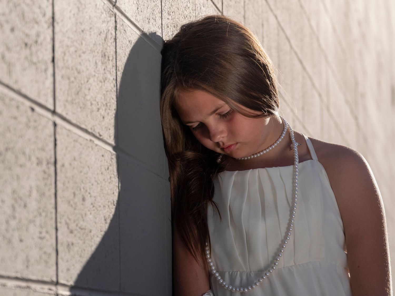 Artistic portrait in white dress and necklace against concrete wall.