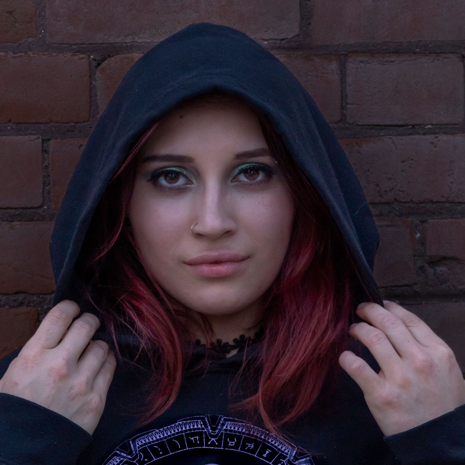 Portrait in black hooded sweatshirt against brick wall background.