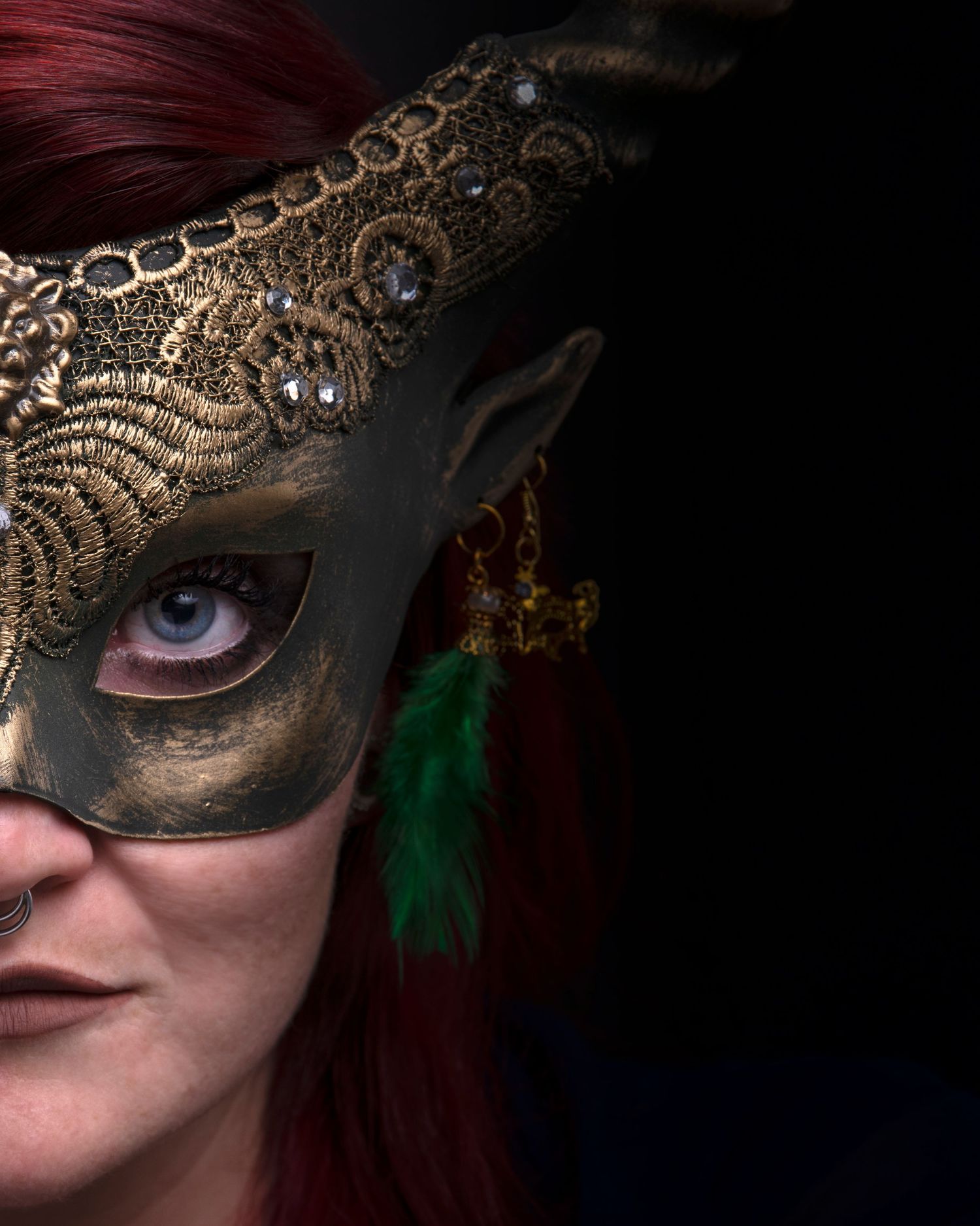 Close-up of an ornate gold masquerade mask with feather details against a dark background.