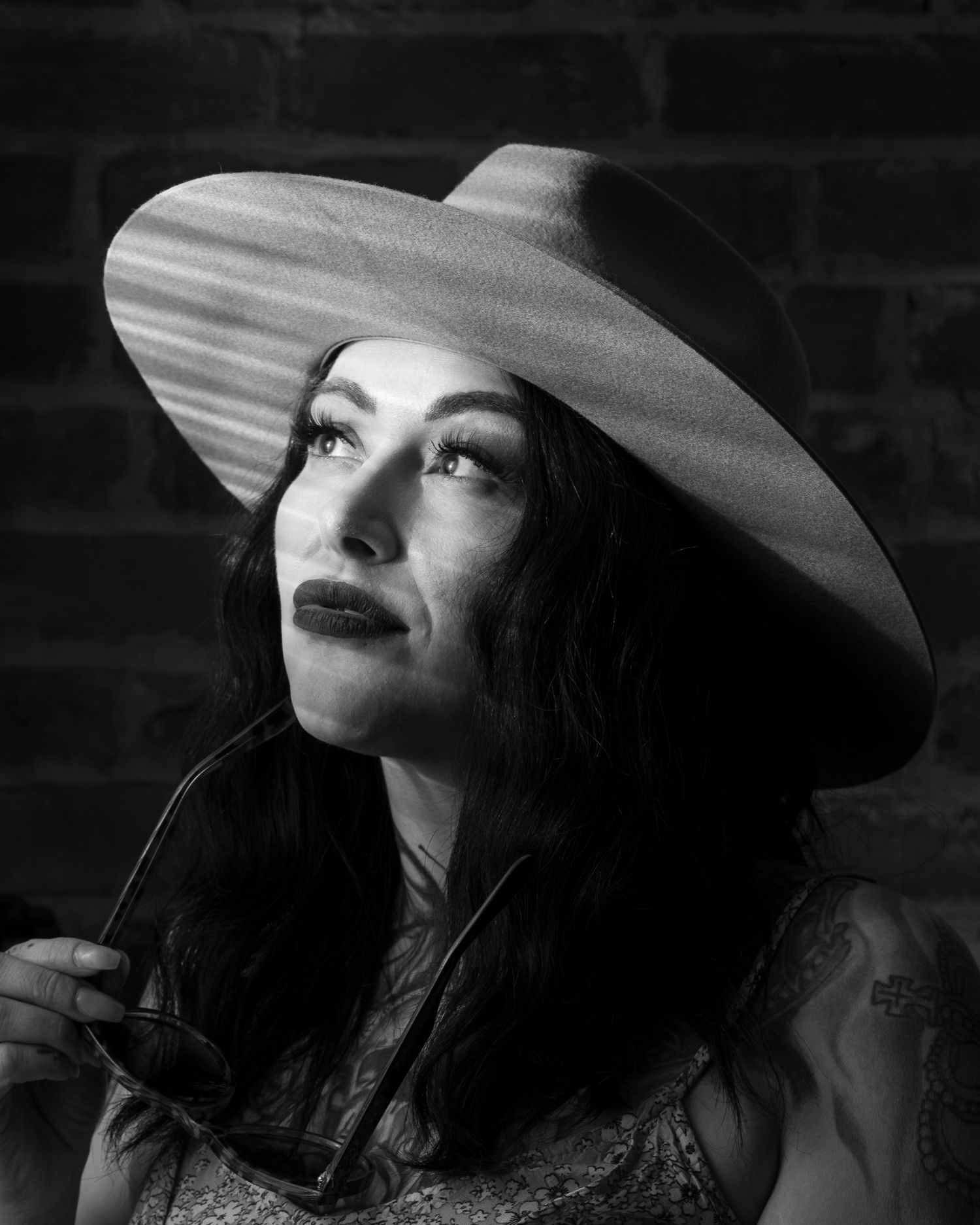 Dramatic black and white portrait wearing wide brim hat against brick wall.