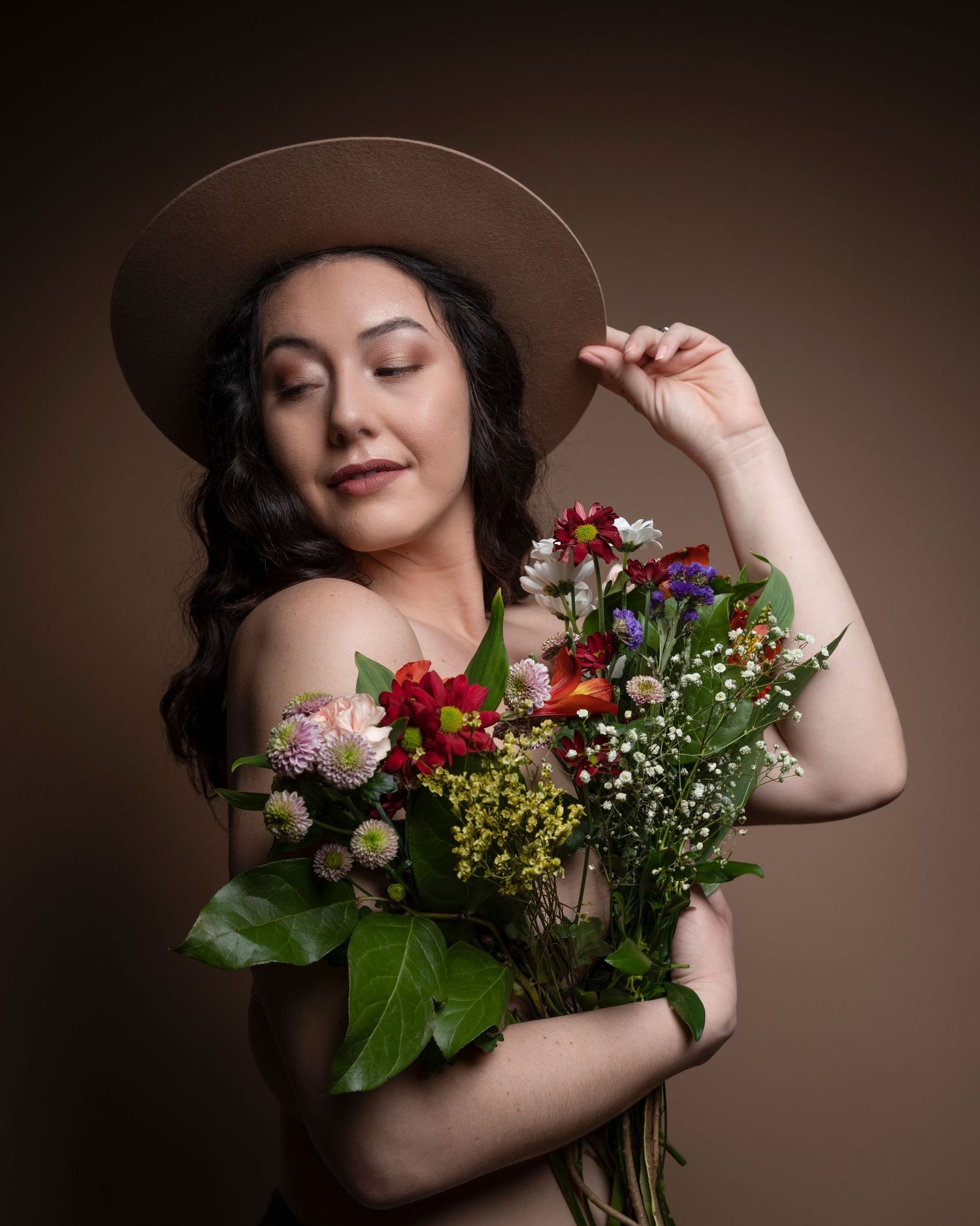 Artistic portrait featuring someone in a brown hat holding fresh flowers against a sepia background.