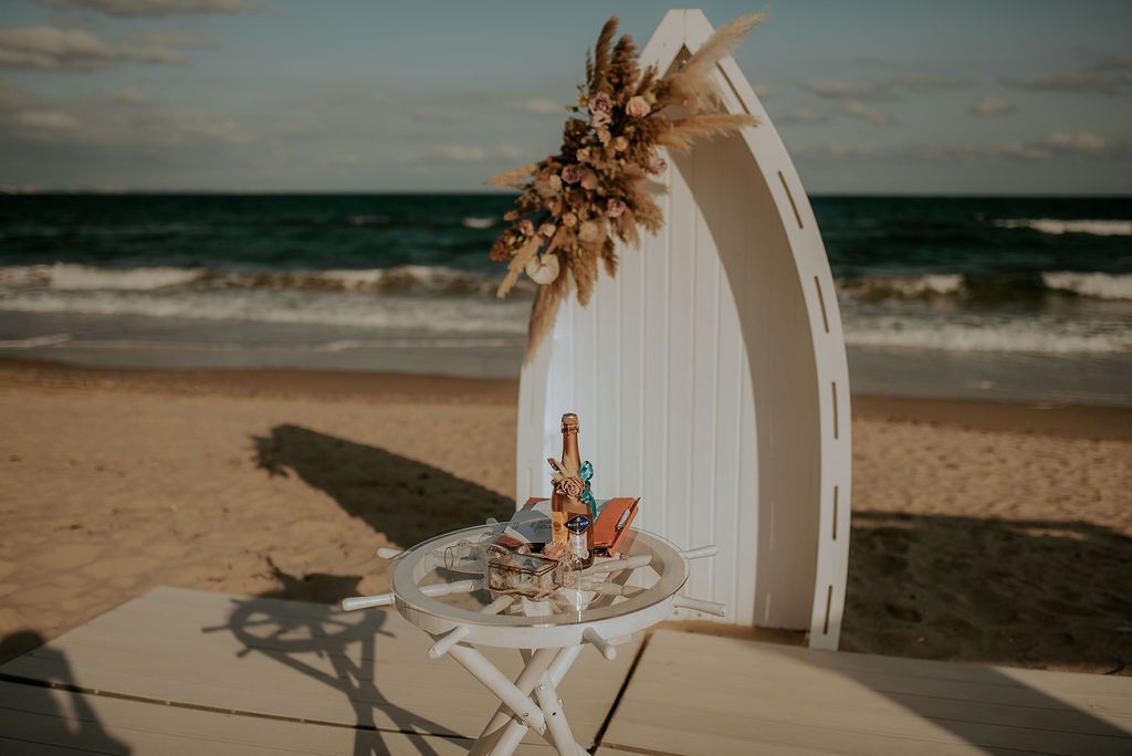 Beach wedding ceremony setup with white arch and chairs overlooking the ocean.