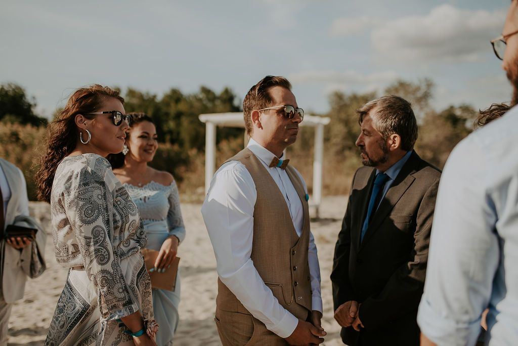 Wedding party members gather on sandy beach during sunset celebration.