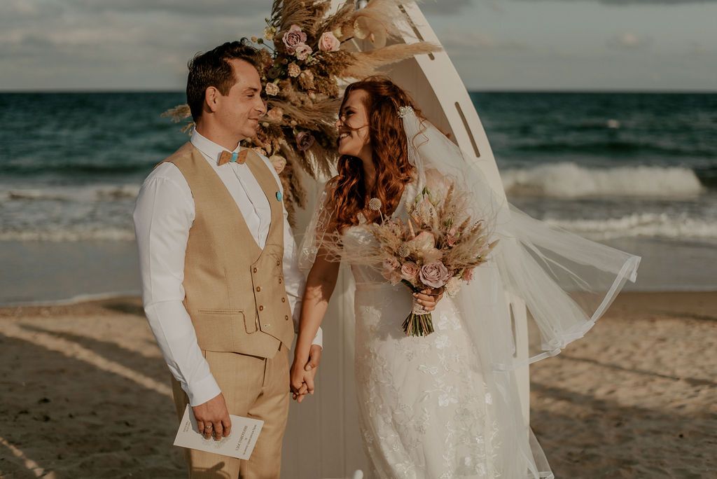 A couple exchanges vows during their intimate beachfront wedding ceremony with dried floral arrangements.
