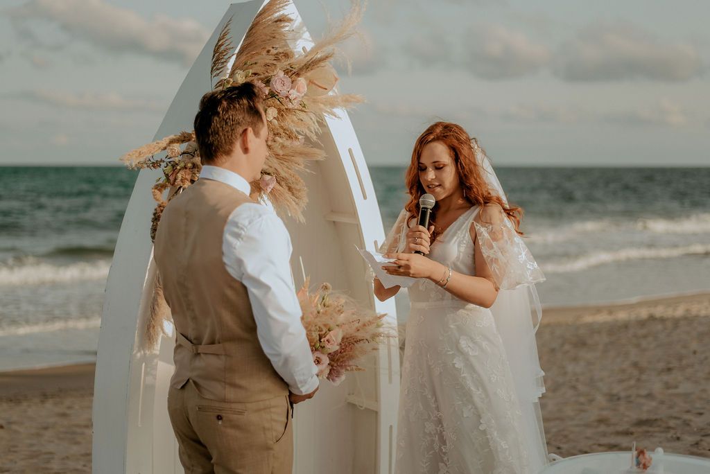 Newlyweds share an intimate moment during their beach wedding ceremony with waves crashing in the background.