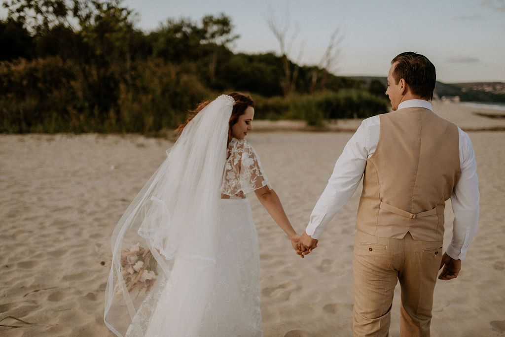 A romantic beach wedding photoshoot at sunset with a couple embracing on the sand.