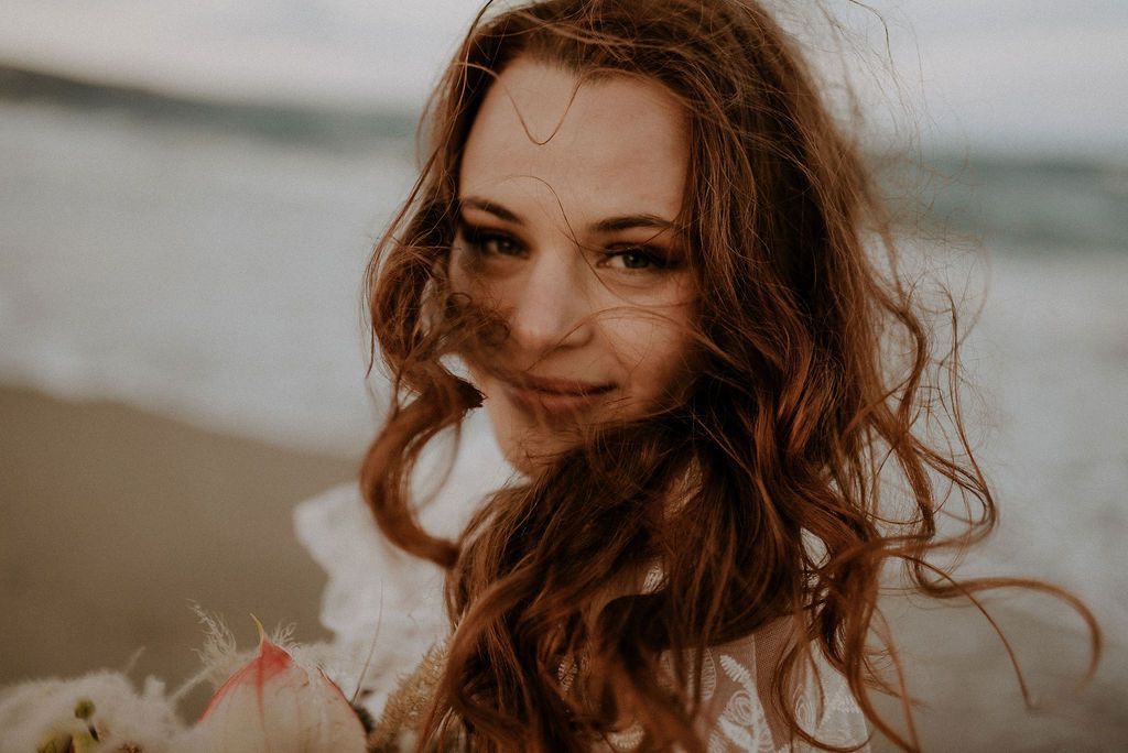 Close-up portrait with windswept hair against a moody beach backdrop.