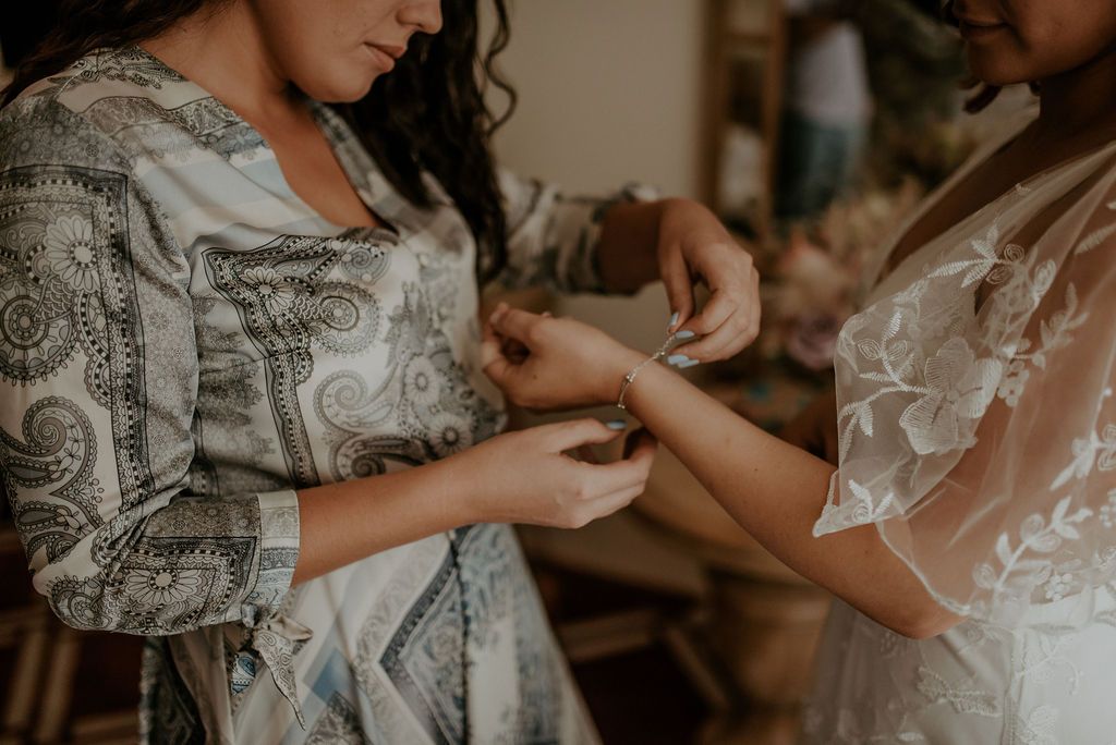 Close-up shot of hands helping with wedding dress preparations in warm moody lighting.
