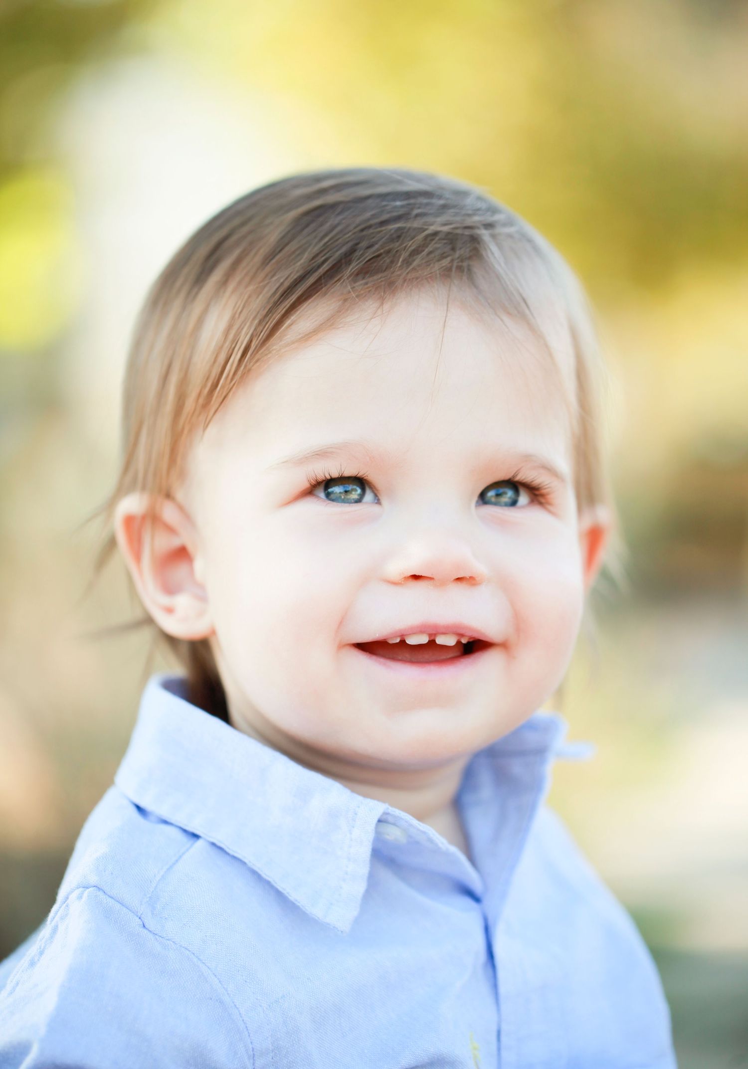 Close up portrait of a smiling child with bright blue eyes wearing a light blue collared shirt.