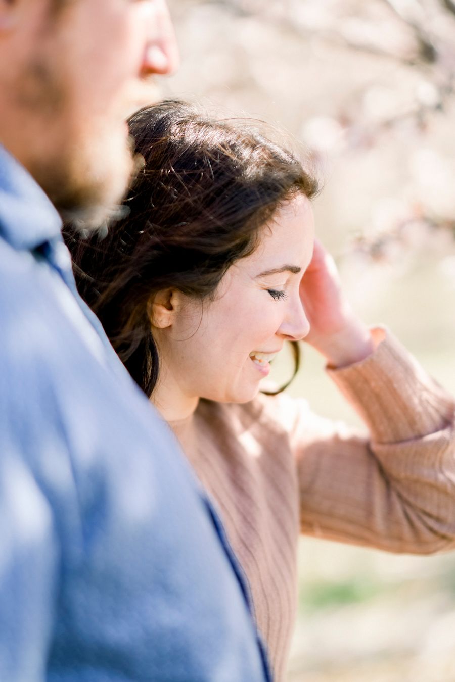 Side profile of a woman laughing joyfully outdoors on a sunny day.