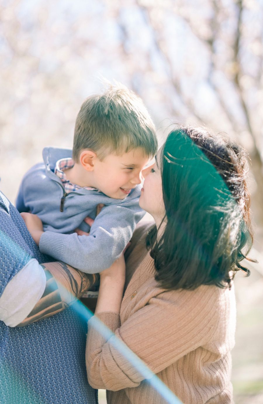 Intimate family moment captured outdoors with spring blossoms in the background.