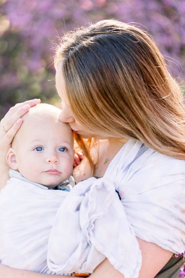 Tender moment between parent and baby against purple flowering trees.