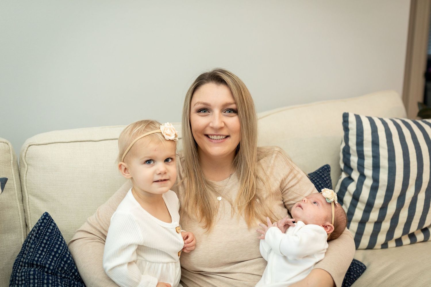Parent poses on couch with toddler and newborn for family photo.