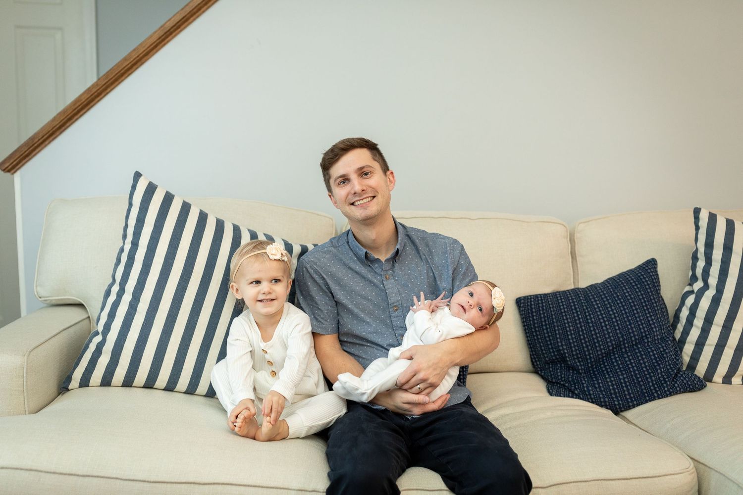 Parent sits on striped couch with toddler and newborn.