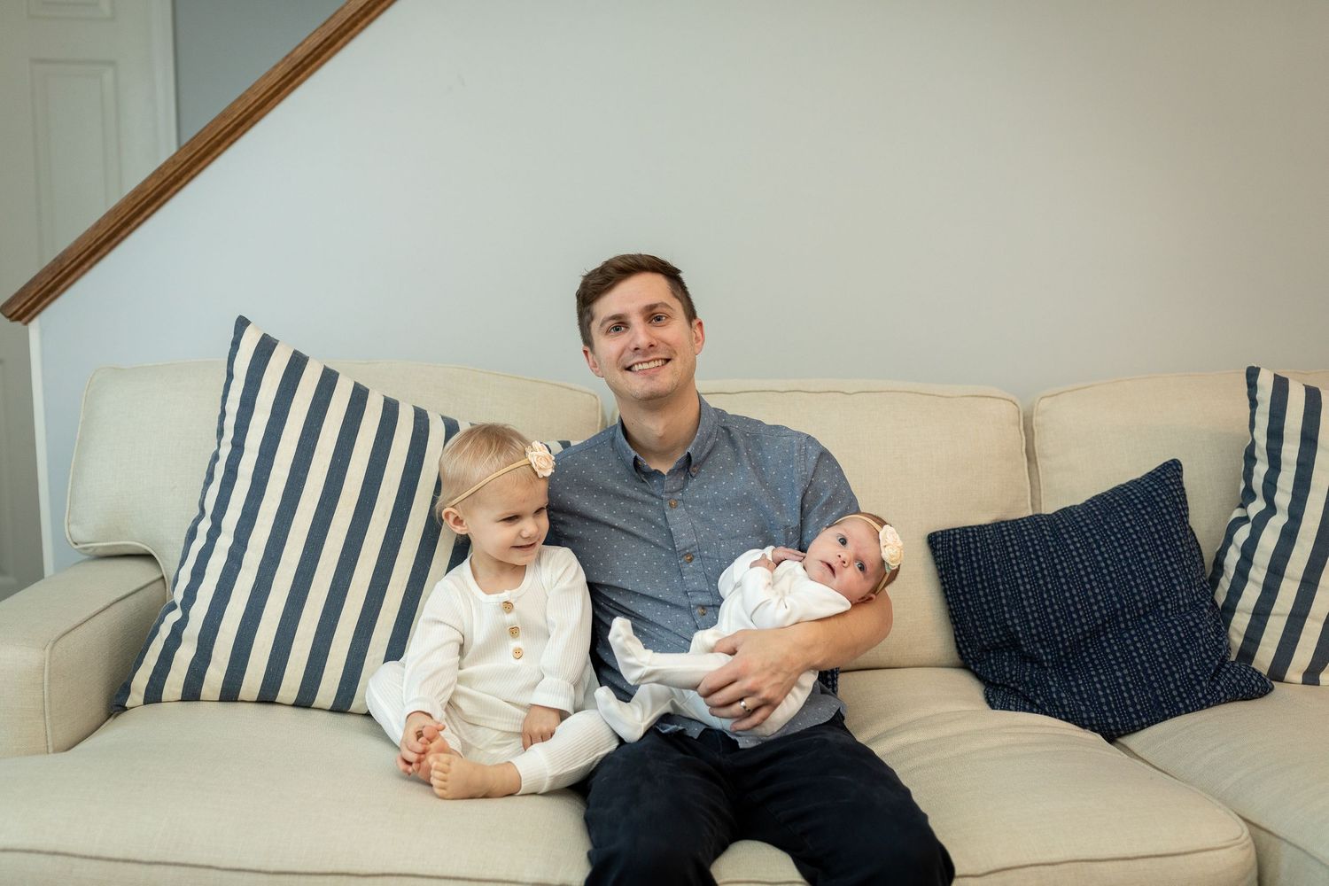 Parent poses with children on beige sofa with blue striped pillows.