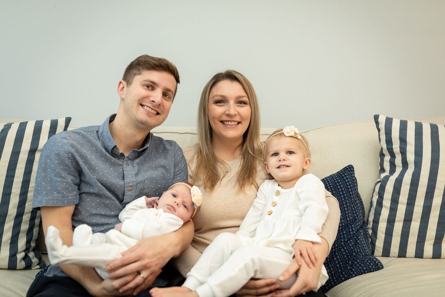Family sitting together on a blue striped sofa with their two young children.