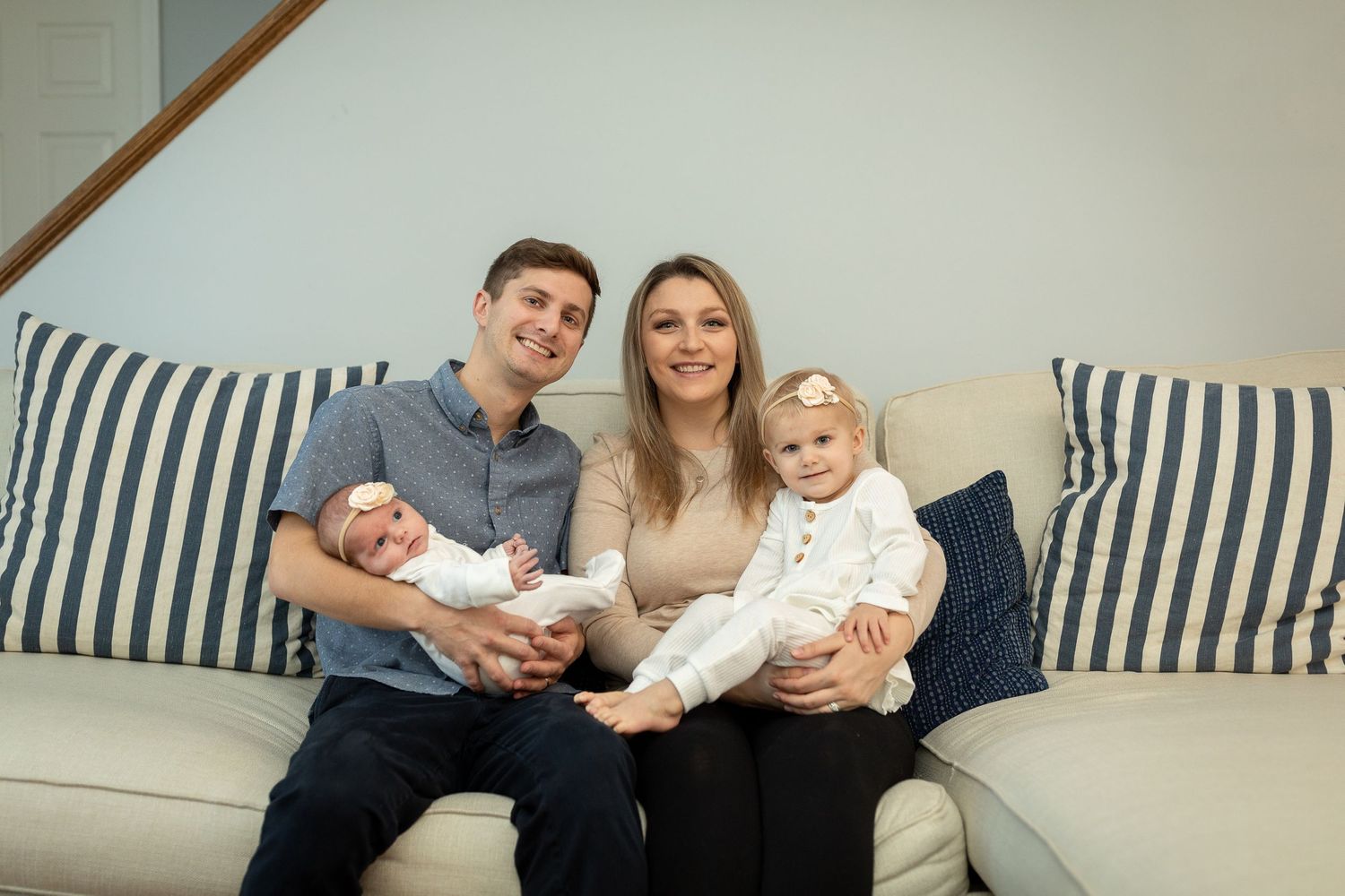 A family relaxes together on a striped couch with their baby and toddler.