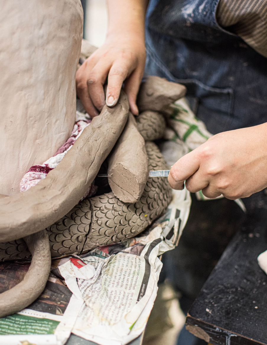 Close-up of hands working with clay on a pottery wheel with newspaper underneath.
