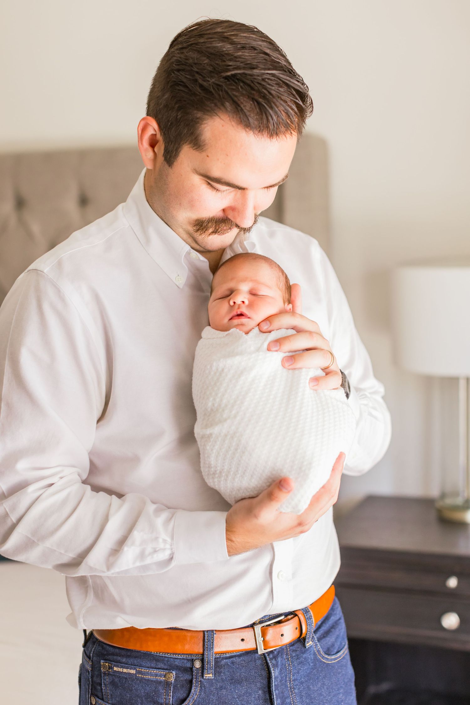 Parent in white shirt tenderly holding sleeping newborn wrapped in white blanket.